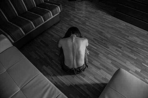 Young depressed sensual female sitting on floor with naked back