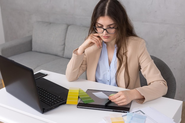 A young designer girl sitting at a table draws on a tablet Makes business calculations on the computer