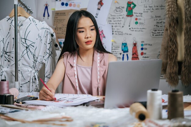 Young designer use laptop computer to search idea while drawing sketch the fashion clothes on paper