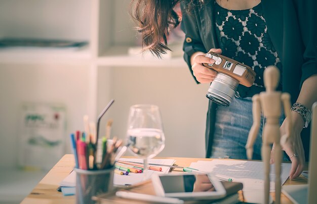 young designer woman working with paperwork and holding digital camera 