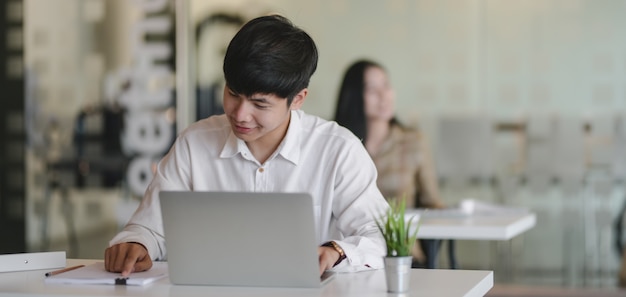 Young designer working on his project with his coworker in the background