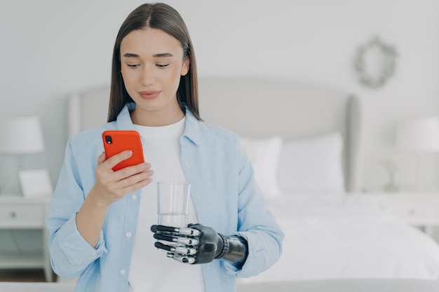 Young disabled girl holds smartphone and glass of water in hands using high tech bionic prosthesis