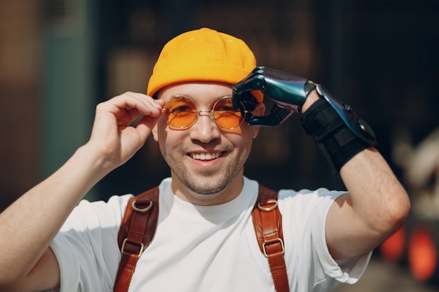 Young disabled man portrait put on yellow glasses with artificial prosthetic hand .