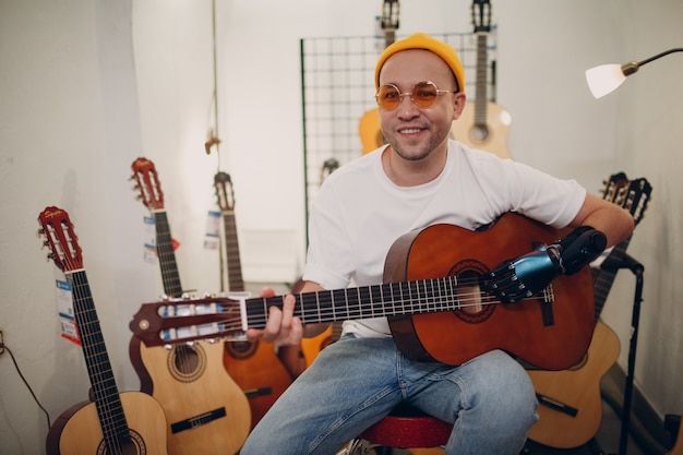 Young disabled man with artificial prosthetic hand plays on guitar at shop