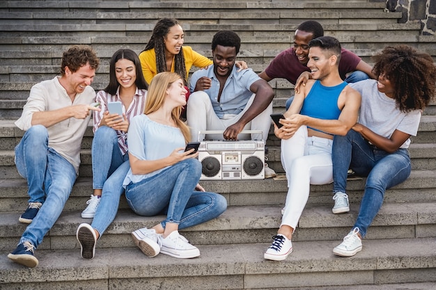 Young diverse people having fun listening music with boombox stereo outdoor in the city - Focus center african girl face