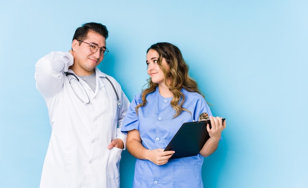 Young doctor couple posing in a blue wall isolated suffering neck pain due to sedentary lifestyle.