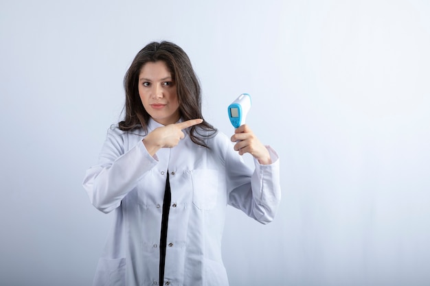 young doctor holding thermometer on white wall. 