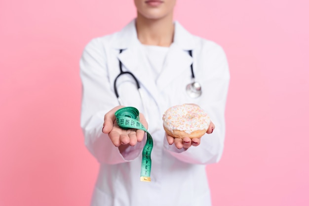 Young Doctor is Holding Donut and Measuring Tape in Room.