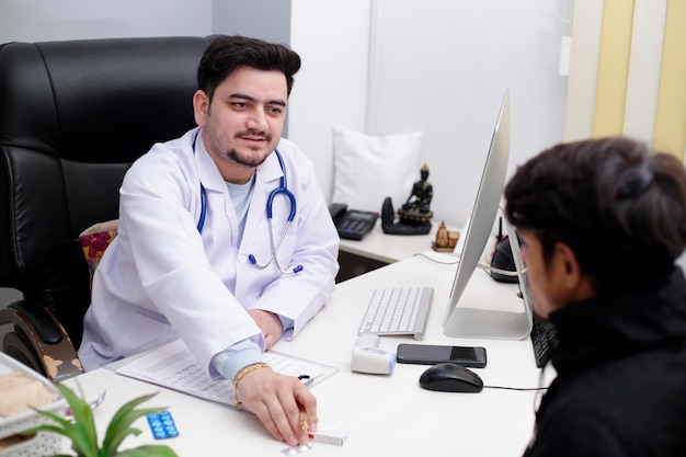 A young doctor is sitting in the clinic with patient and giving medicine to him