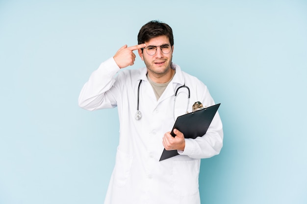 Young doctor man isolated on blue wall showing a disappointment gesture with forefinger.