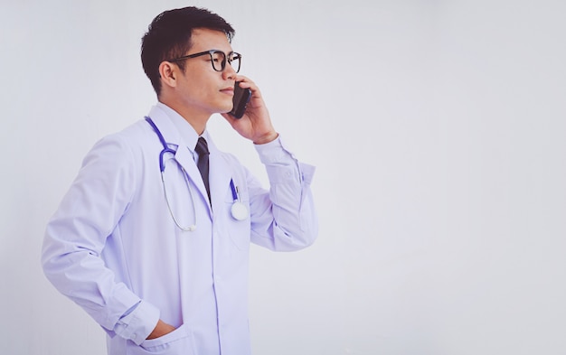 Young doctor man wearing a white coat using a smartphone