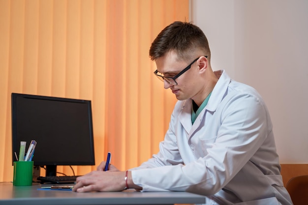 Young doctor sits at table and writes prescription