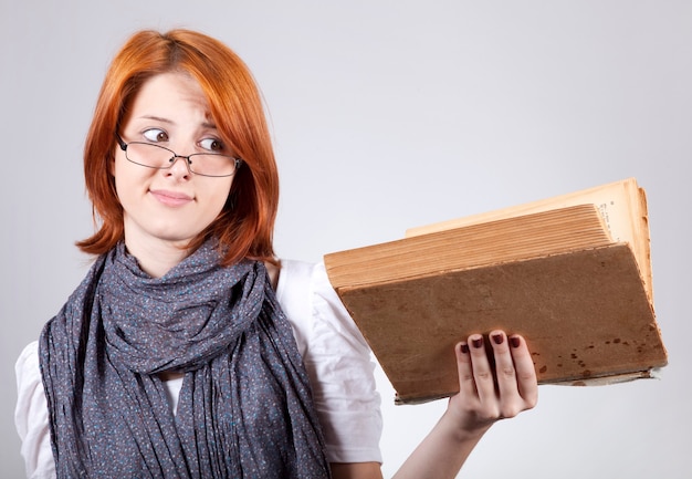 Young doubting fashion girl in glasses with old book