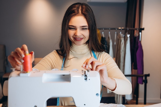 Young dressmaker woman sews clothes on sewing machine