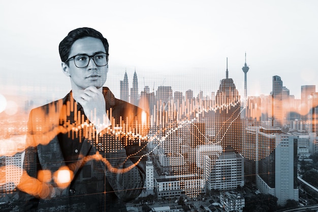 A young eastern handsome trader and stock market analyst in suit dreaming about market behavior and forecast in crisis Trading at corporate finance fund Forex chart Kuala Lumpur Double exposure