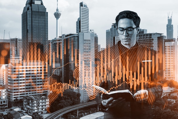 A young eastern handsome trader in suit examine his notes to predict the market behavior based on historic data and stock market Corporate finance fund and forex chart Kuala Lumpur Double exposure