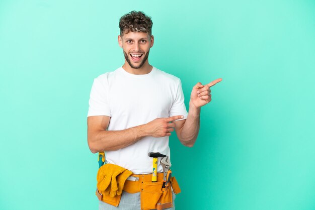 Photo young electrician blonde man isolated on green background surprised and pointing side