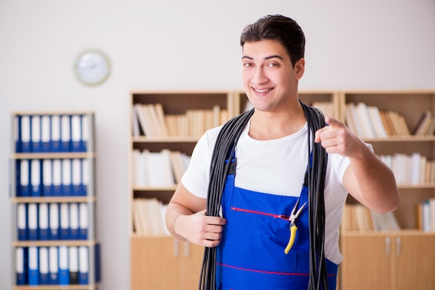 Young electrician with cable working in office