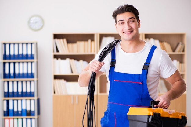 Young electrician with cable working in office