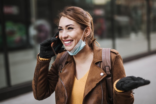 Young and elegant business woman walking on empty city street. She is using phone while wearing protective mask to protect herself from dangerous virus. Corona virus or Covid-19 concept.