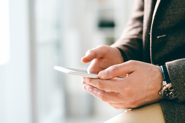 Young elegant businessman with wristwatch holding smartphone while communicating through video-chat or texting