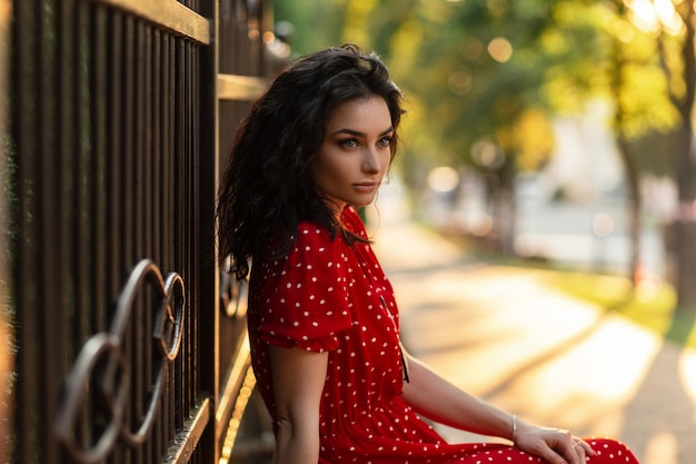 Young elegant curly model woman in vintage red dress sitting and rest  on the street