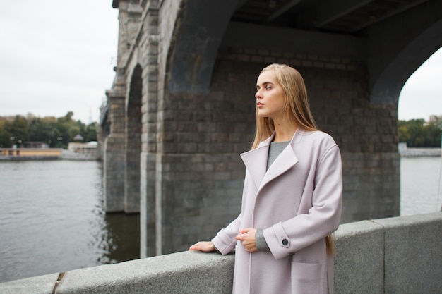 Young elegant stylish fashion woman in gray coat on classic european bridge looking outside