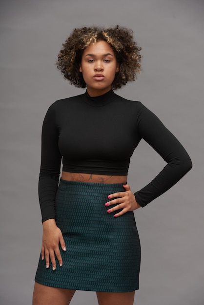 Young elegant woman in cropped top and skirt posing in front of camera