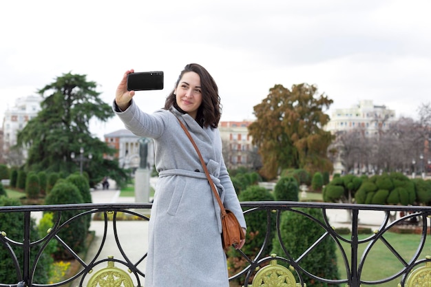 Young elegant woman sightseeing She is taking a picture with her mobile phone of herself in a city garden