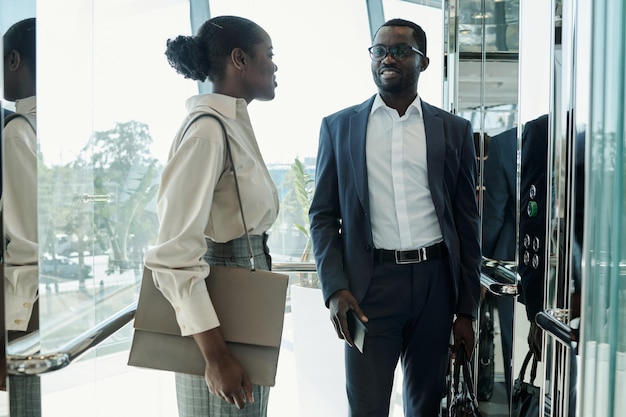 Young elegant woman with handbag and her colleague in suit talking in elevator