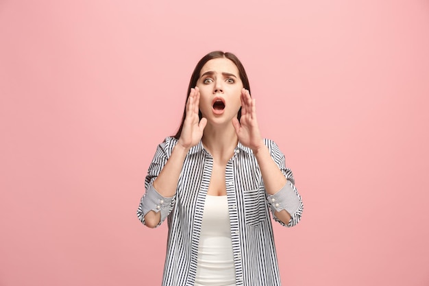 The young emotional angry woman screaming on pink studio background