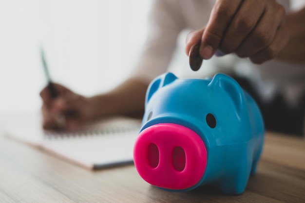 A young employee is putting coins into a blue piggy bank.