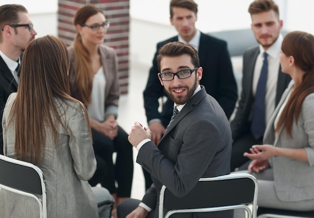 Photo young employee sitting in a circle of colleagues and looking at the camera