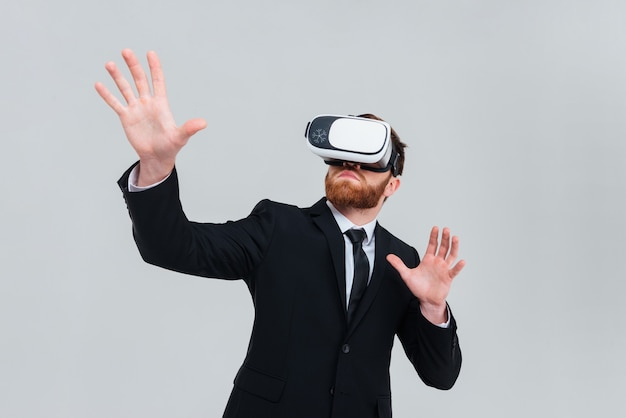 Young engineer in black suit wearing virtual reality device. Isolated gray background