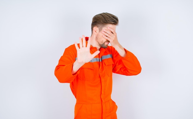 Young engineer man is covering his eyes and showing stop gesture on white background