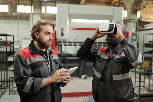 Young engineer scrolling in tablet while standing by colleague in vr headset