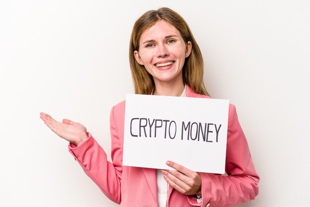 Young English business woman holding a crypto money placard isolated on white background showing a copy space on a palm and holding another hand on waist