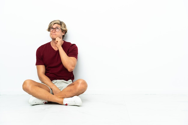 Young English man sitting on the floor having doubts and thinking