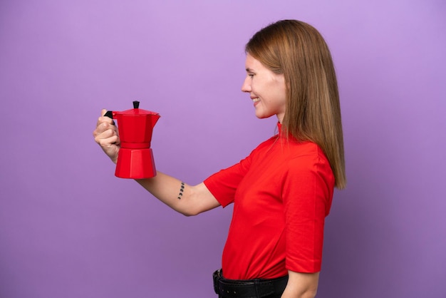 Young English woman holding coffee pot isolated on purple background with happy expression