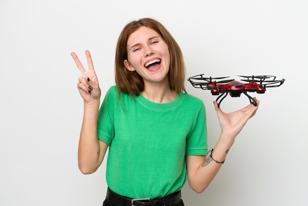 Young English woman holding a drone isolated on white background smiling and showing victory sign