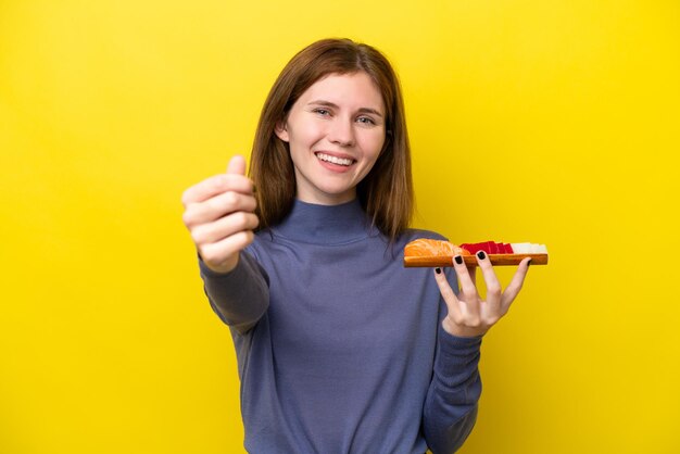 Young English woman holding sashimi isolated on yellow background making money gesture