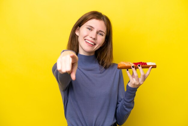 Young English woman holding sashimi isolated on yellow background pointing front with happy expression