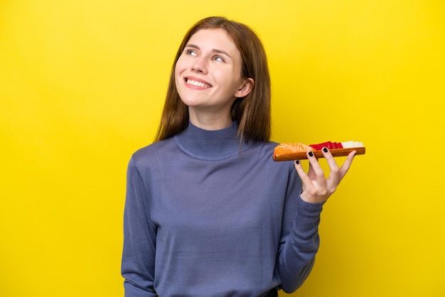 Young English woman holding sashimi isolated on yellow background thinking an idea while looking up