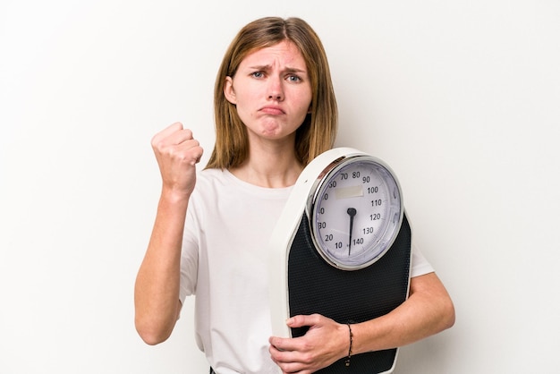 Young English woman holding a scale isolated on white background showing fist to camera aggressive facial expression