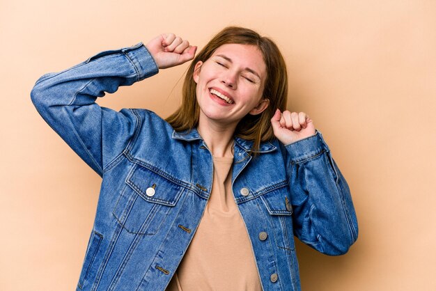 Young English woman isolated on beige background celebrating a special day jumps and raise arms with energy