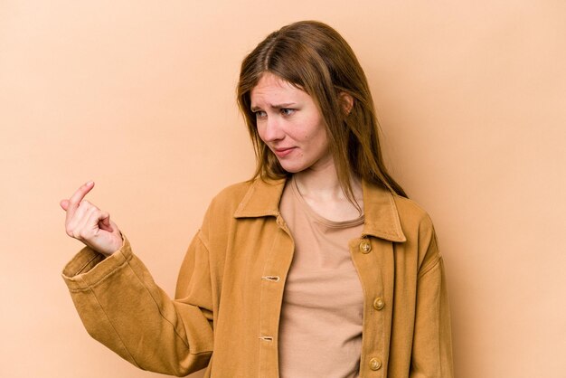 Young English woman isolated on beige background pointing with finger at you as if inviting come closer.