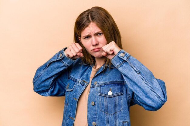 Young English woman isolated on beige background throwing a punch anger fighting due to an argument boxing