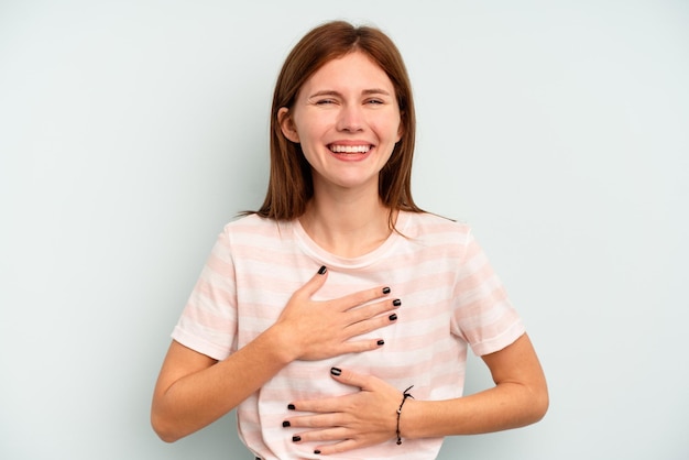 Young English woman isolated on blue background laughs happily and has fun keeping hands on stomach