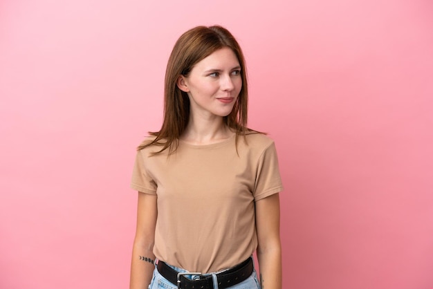 Young English woman isolated on pink background having doubts while looking side