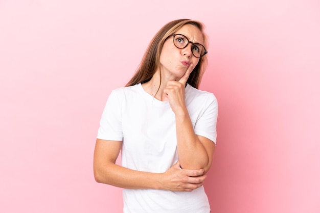 Young English woman isolated on pink background having doubts while looking up